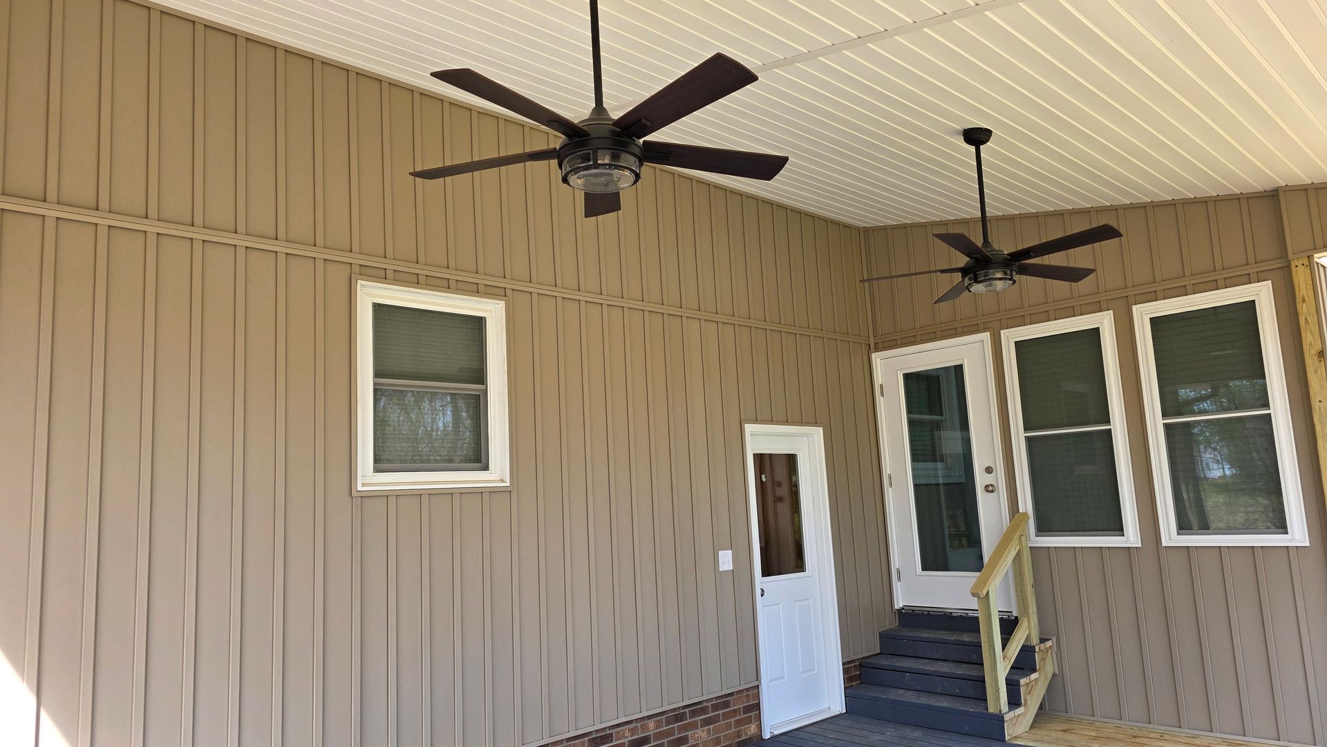 There are two ceiling fans on the porch of a house.