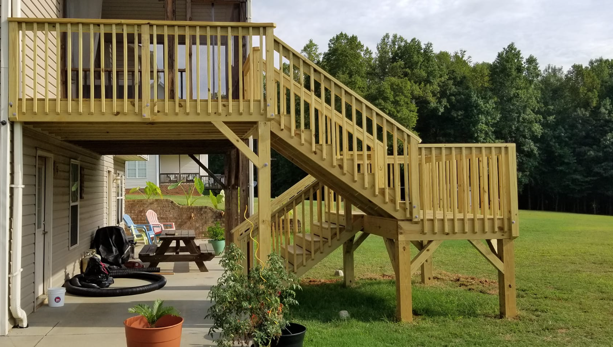 Wooden deck with stairs leading down to a grassy yard. A small table, chairs, and a baby stroller are visible below the deck.