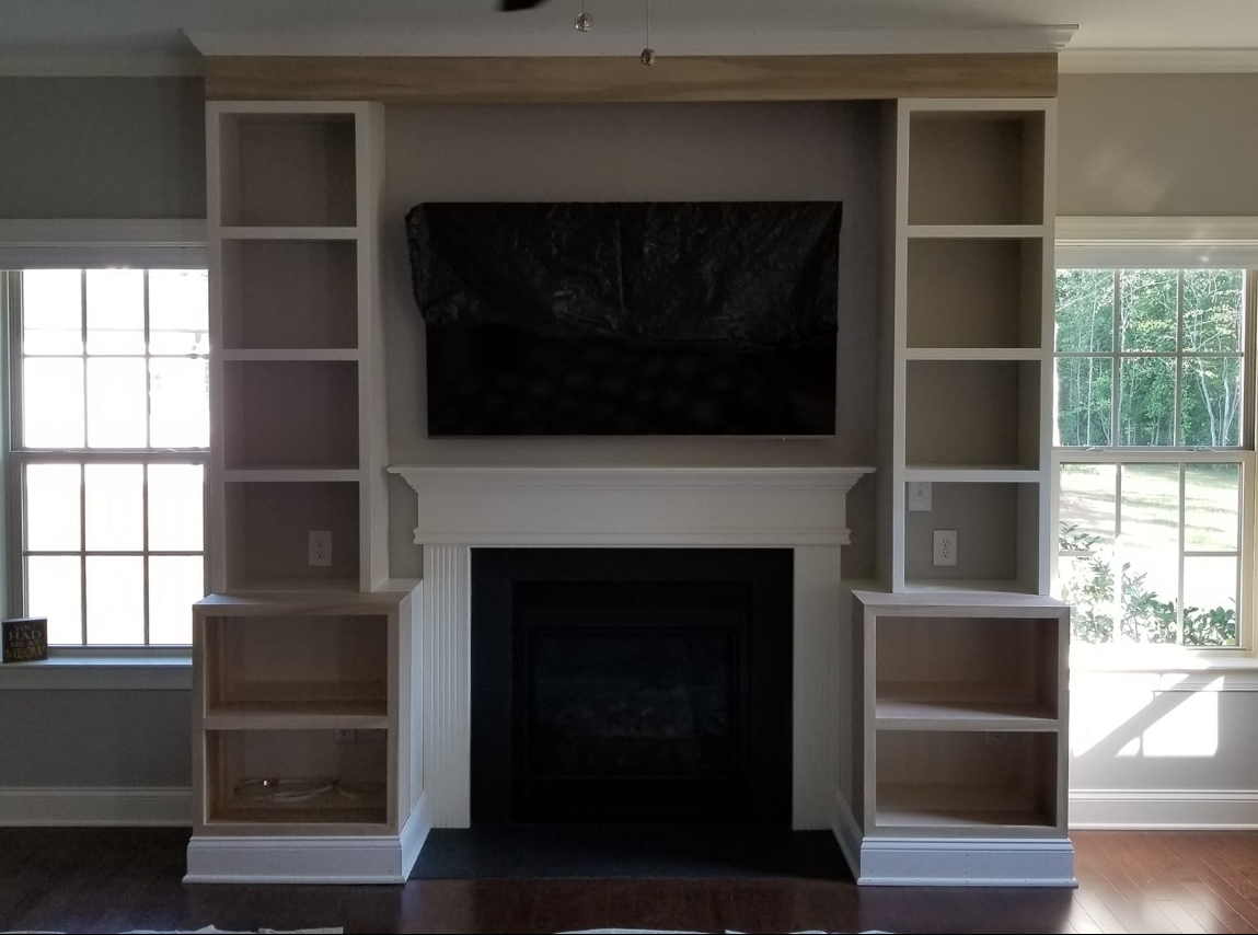 Built-in fireplace with bookshelves and a TV mounted above the mantel; windows flank the structure, with hardwood flooring.