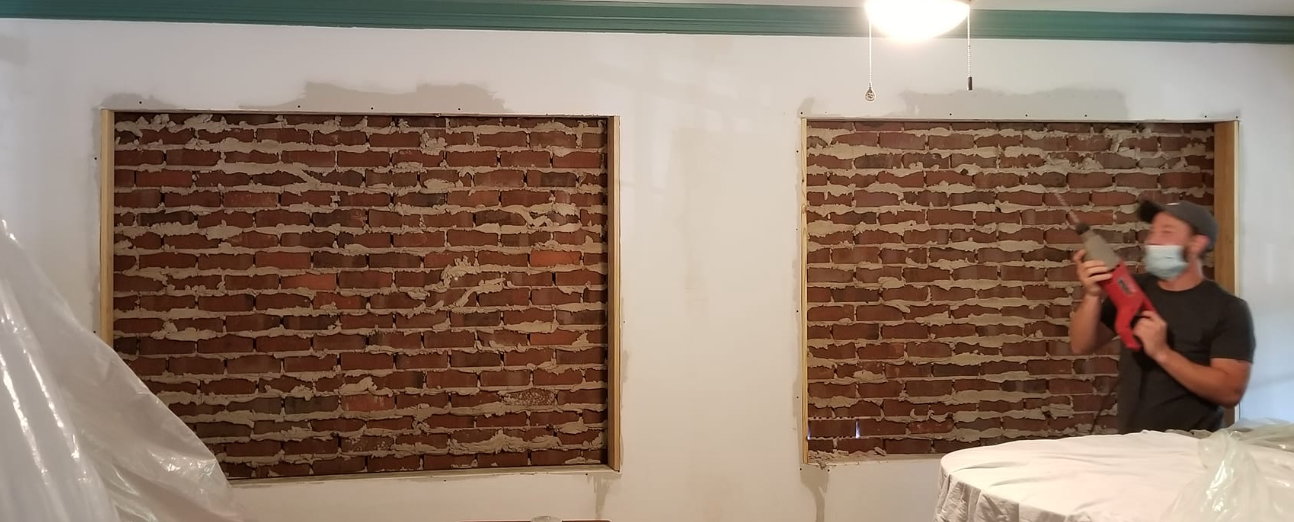 A man wearing a mask is standing in front of a brick wall.