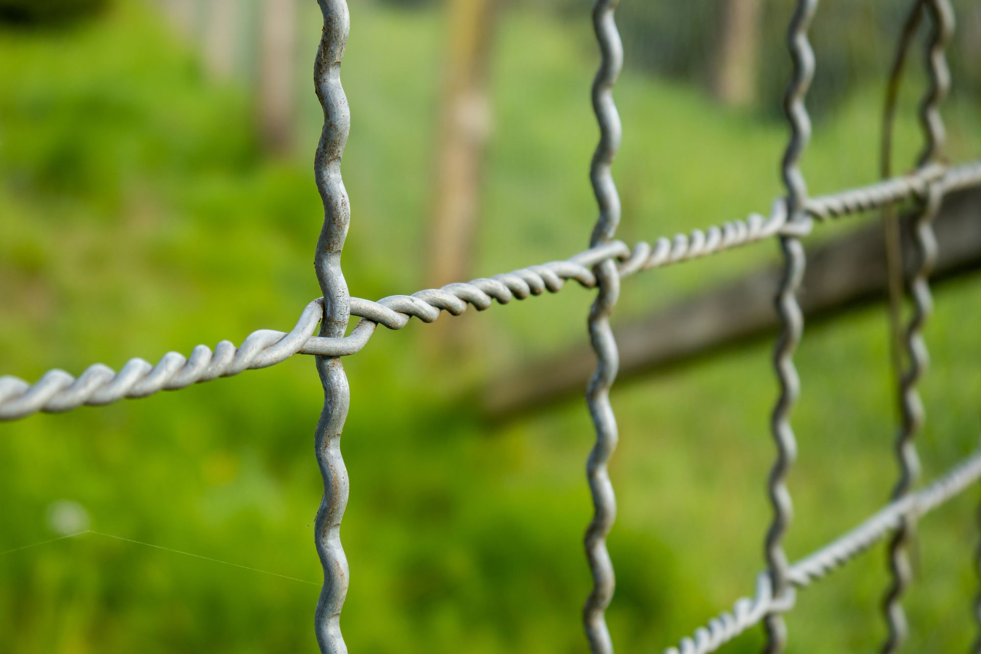 Close-up of a woven metal wire mesh fence outdoors.