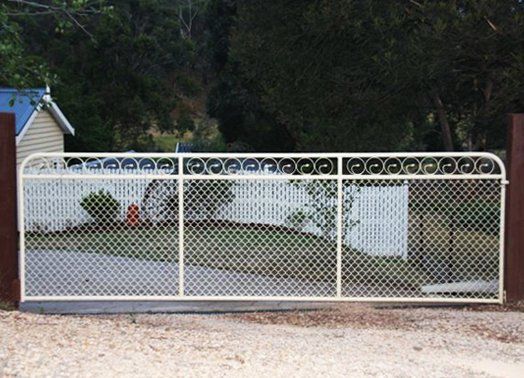 Beige metal driveway gate with diamond mesh and decorative top, set between brown posts.