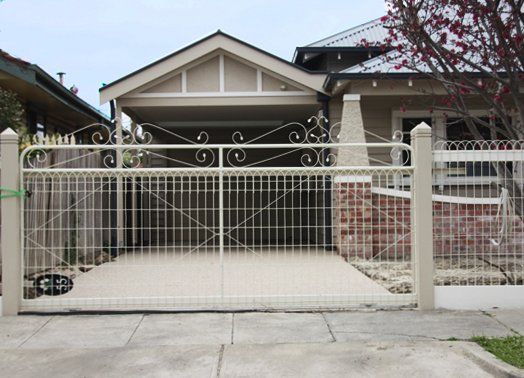 Beige house with a driveway behind a beige metal gate on a city street.