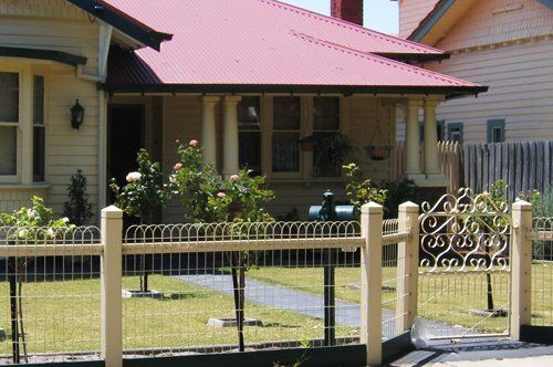 Beige Victorian home with pink roof and ornate fence.
