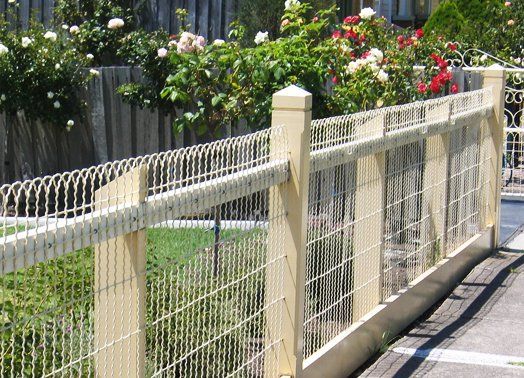 Wooden fence with wire mesh, bordering a garden of roses on a sunny day.