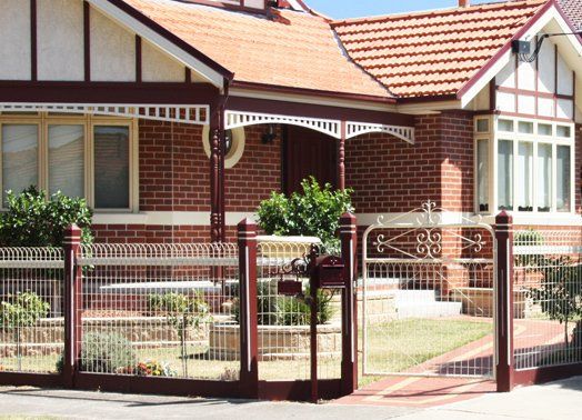 Brick home with terracotta roof, arched porch, ornate fence, and green lawn.