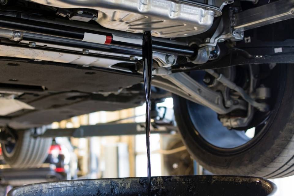 Oil draining from a car's undercarriage into a black catch basin during a maintenance service.