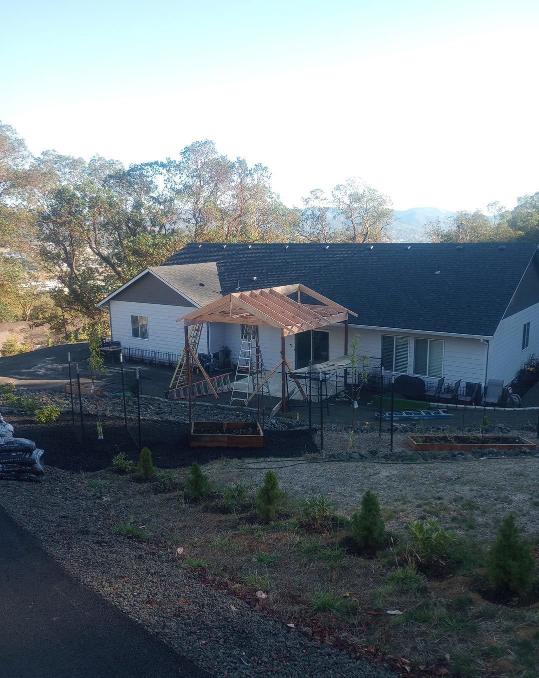 Rural farmhouse with white walls and red roof, seen behind a fence and trees on a sunny day