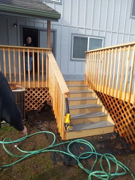 Wooden stair ramps leading to a gray house porch, with lattice skirting and a green hose on muddy ground.