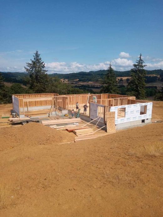 Partially built house foundation on a dirt lot under a clear sky, with wooded hills in the background