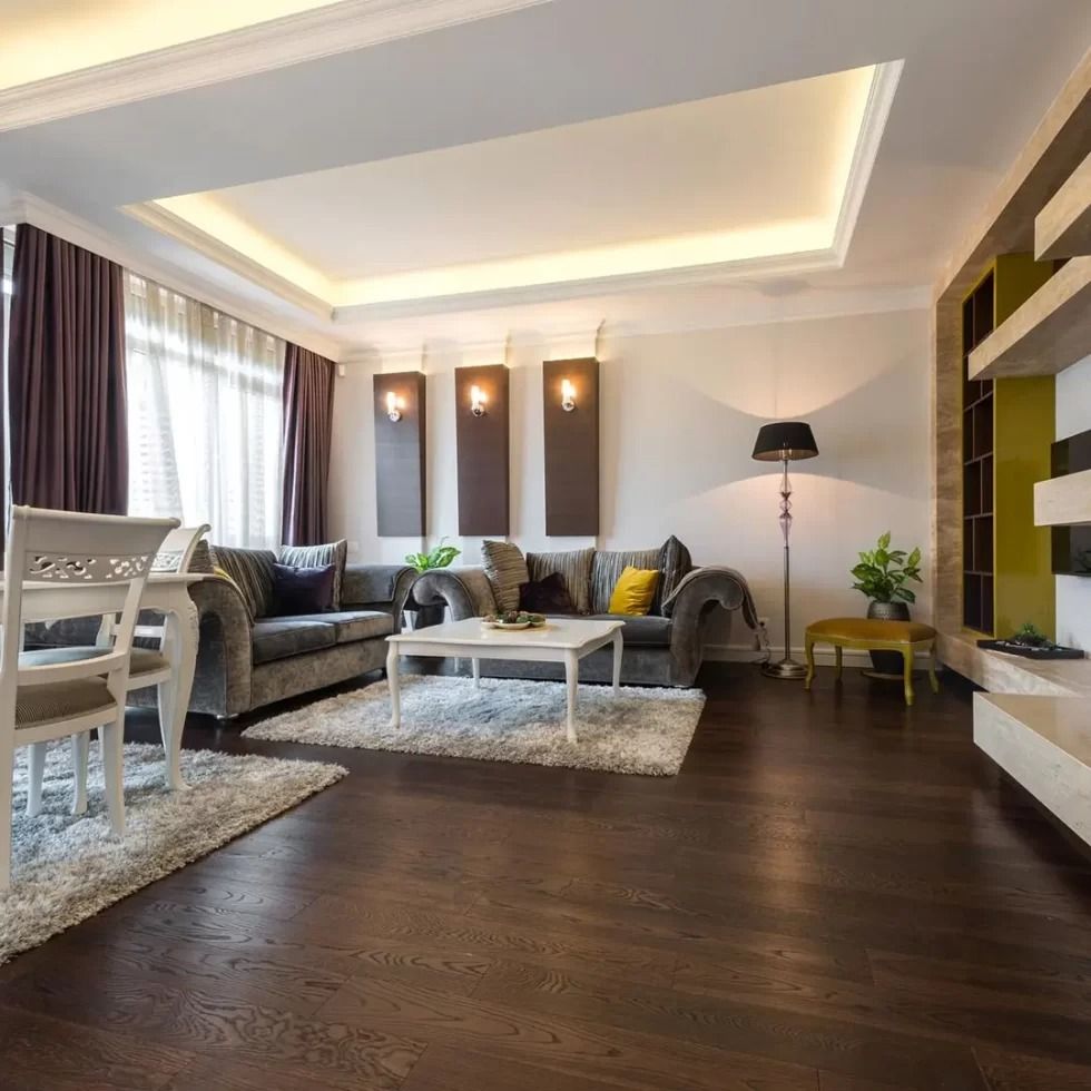 Modern living room with dark wood floors, white sofa, gray armchairs, and soft recessed lighting