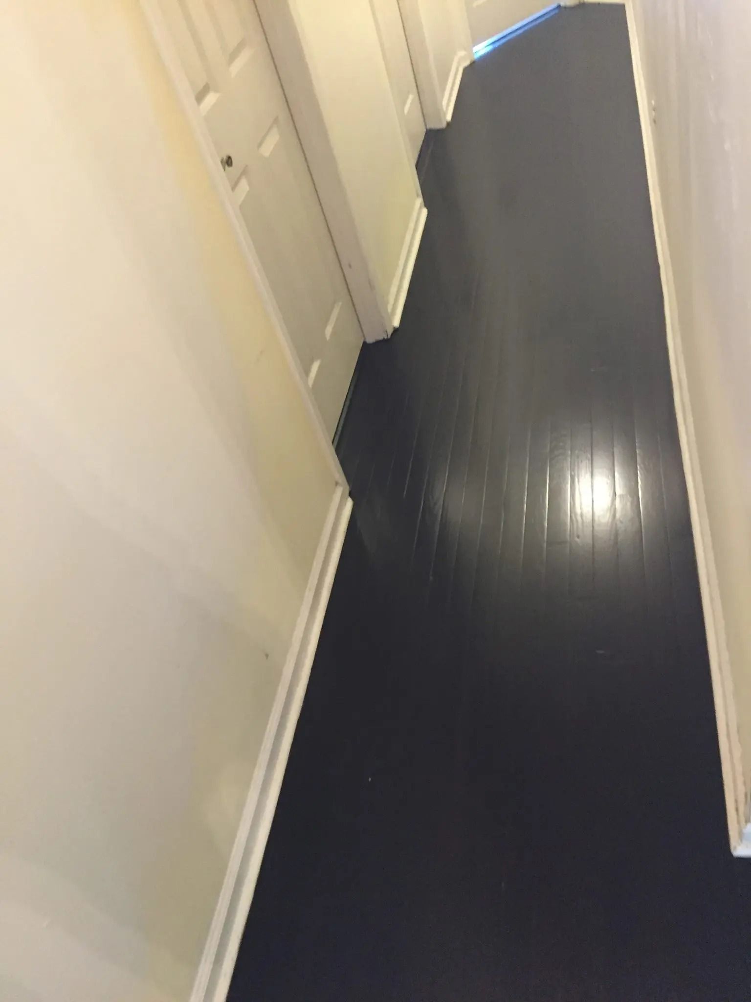 Narrow hallway with white doors and dark floor, viewed at an angle.