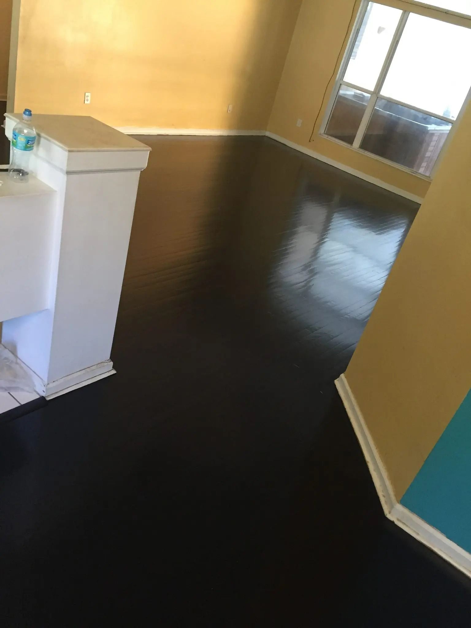 Empty hallway with yellow walls, dark floor, and a window at the end.