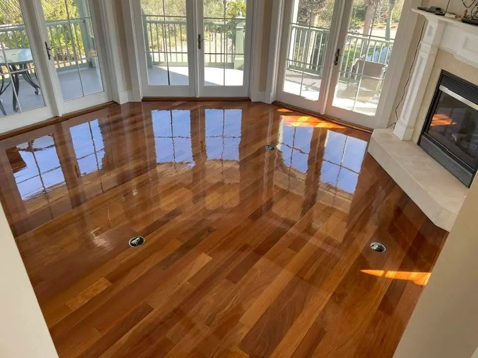Sunlit hardwood floor in a bright room with large windows and a fireplace
