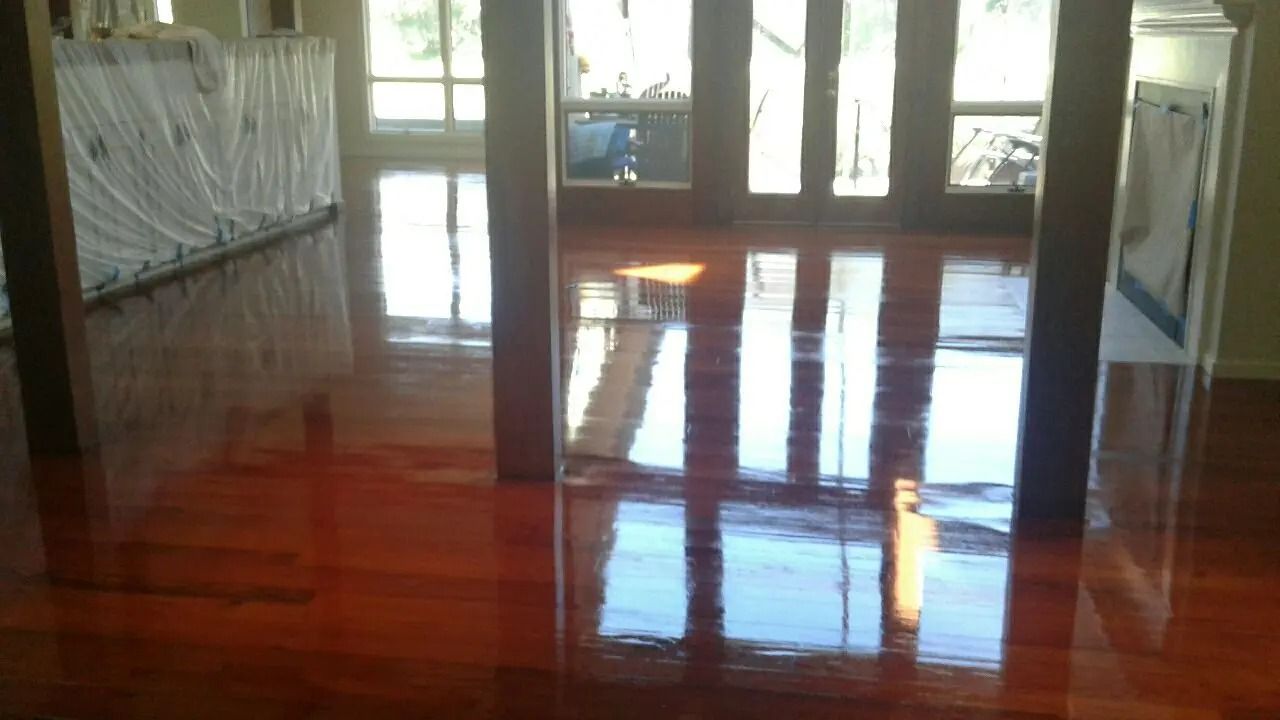 Empty room with glossy wooden floor, large windows, and covered furniture along the walls