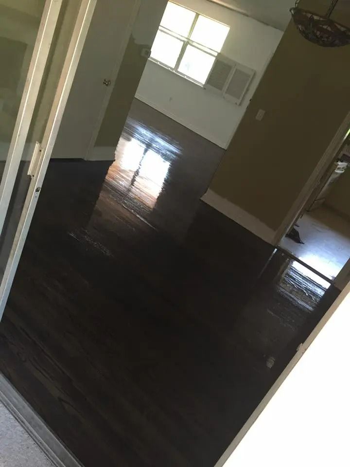Empty room with dark hardwood floors, white walls, and sunlight from a window.