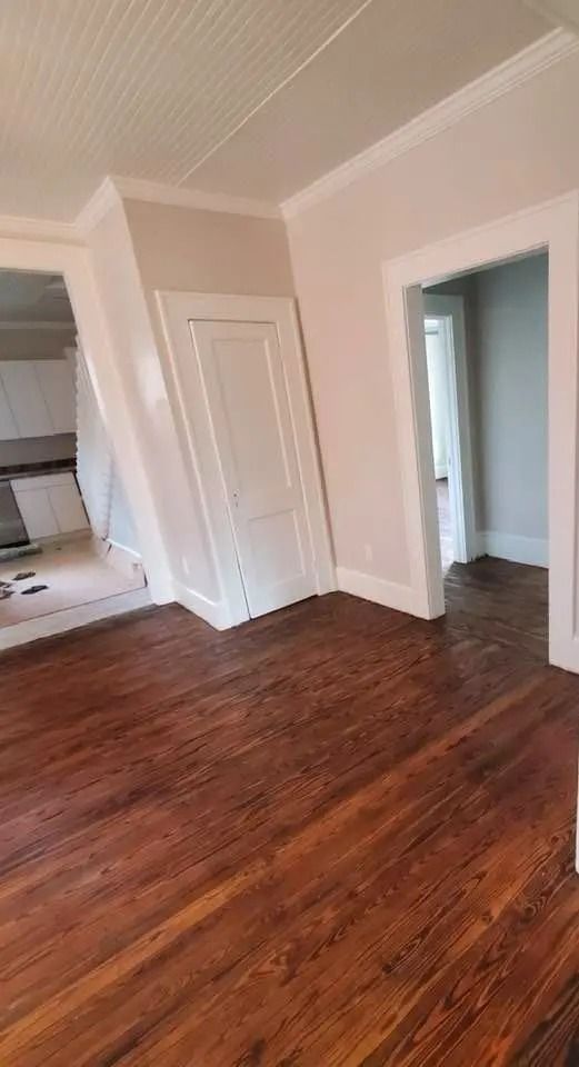 Empty room with dark hardwood floors, white walls, and open doorways.