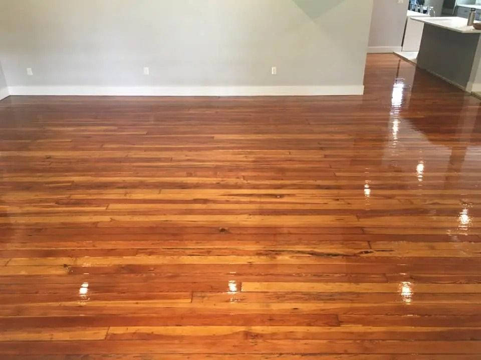 Empty polished hardwood floor in a sparsely furnished room with white walls.