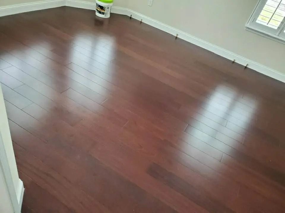 Empty room with glossy reddish-brown hardwood floor and white baseboards.