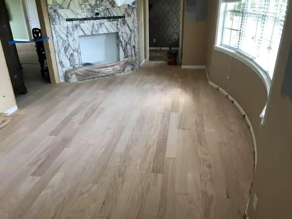 Empty living room with light wood floor, marble fireplace, and large curved window.