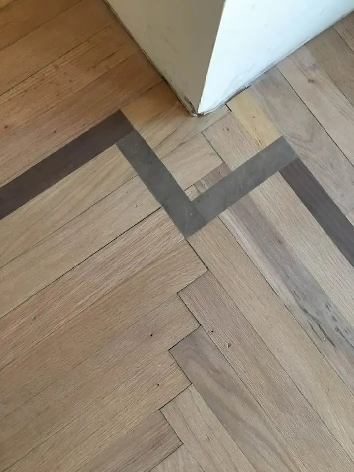 Close-up of a wood floor with dark inlaid border near a white wall corner