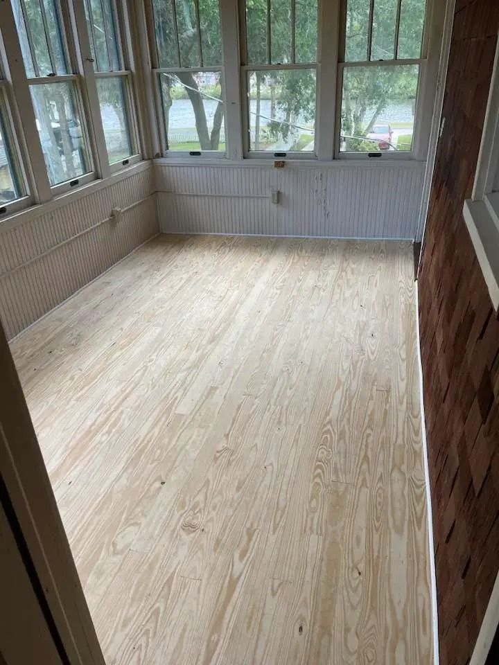 Empty sunroom with light wood floors, large windows, and a wainscoted wall.