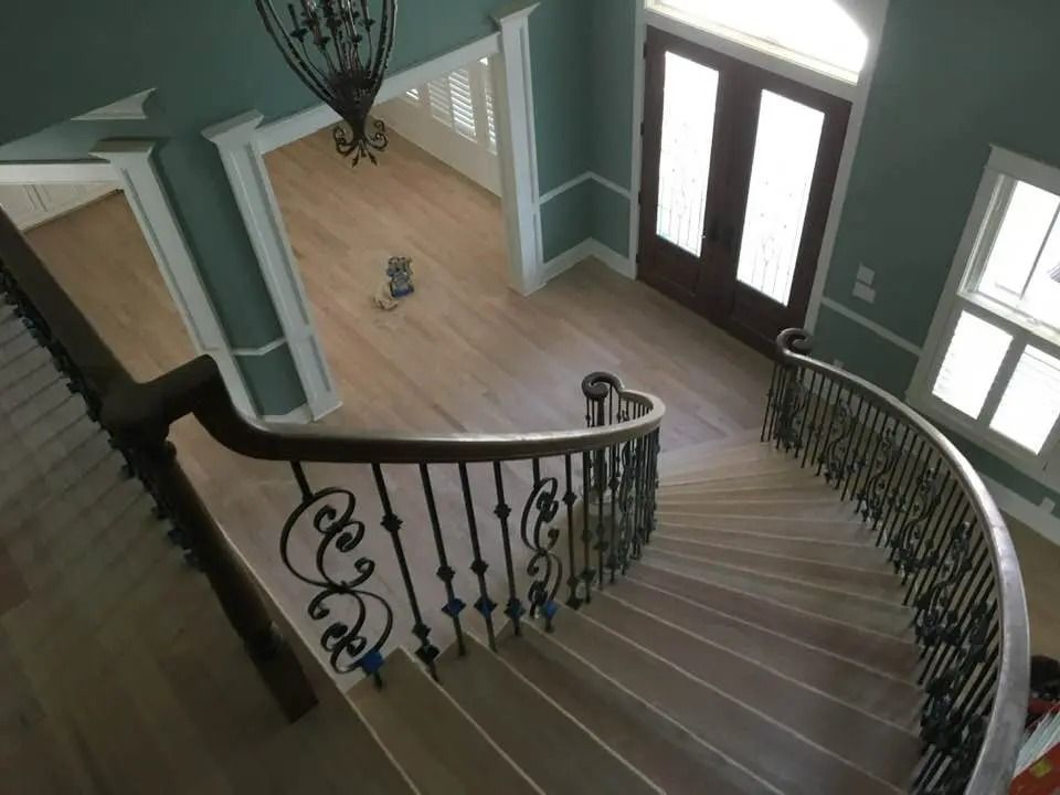 Curved staircase with dark iron railing in a bright foyer with teal walls and wood floors