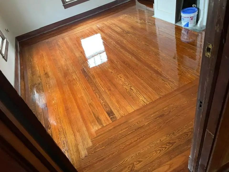 Shiny hardwood floor in a room, with a white square reflection near the center.