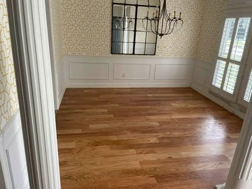Empty dining room with hardwood floor, patterned wallpaper, white wainscoting, mirror, and chandelier