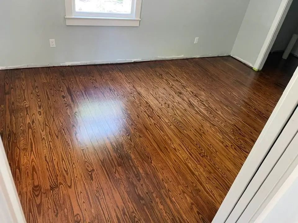 Empty room with glossy hardwood floors, gray walls, and a window letting in light