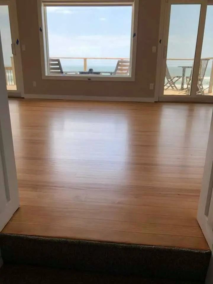 Empty living room with wood floor, large windows, and ocean view beyond a balcony.