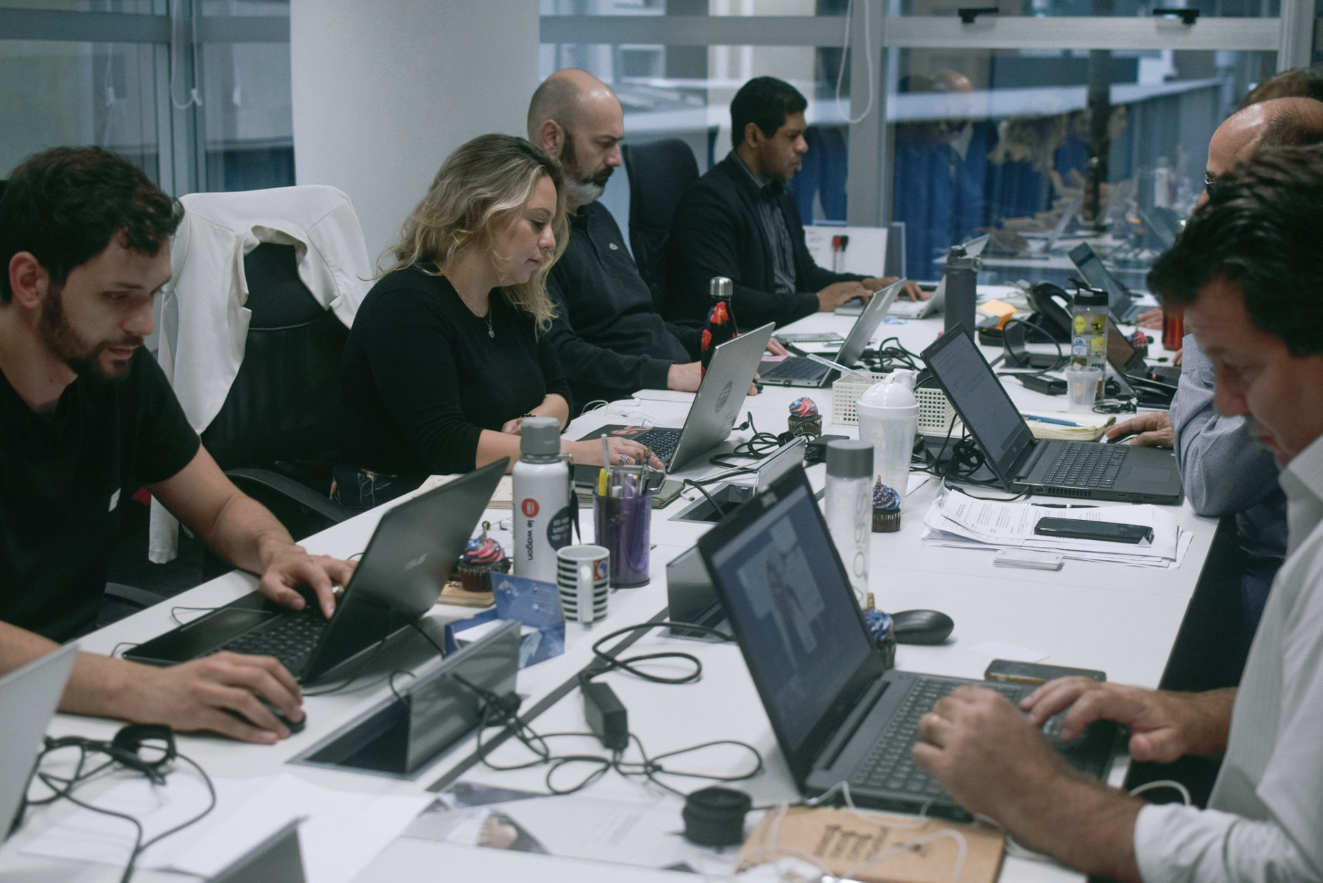 A group of people are sitting at a long table using laptops.
