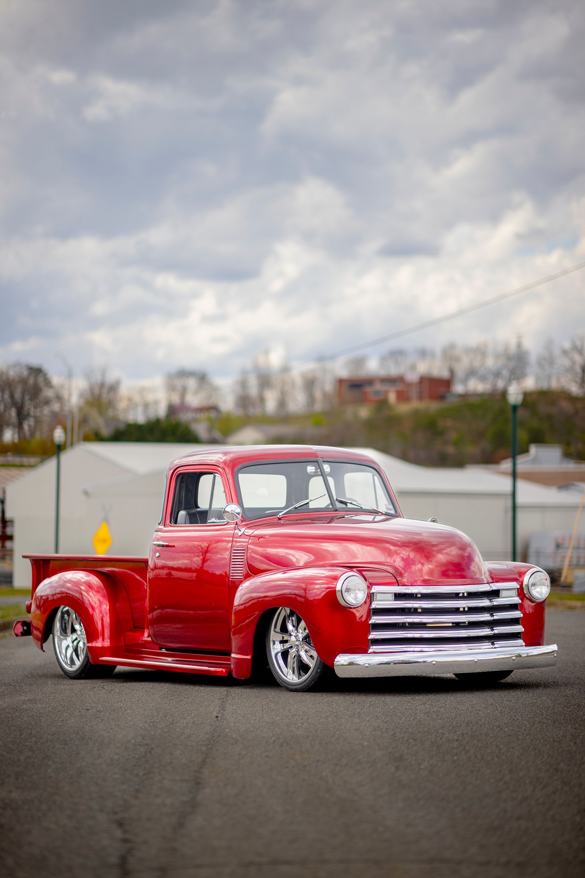 Red vintage pickup truck parked outdoors on pavement under a cloudy sky