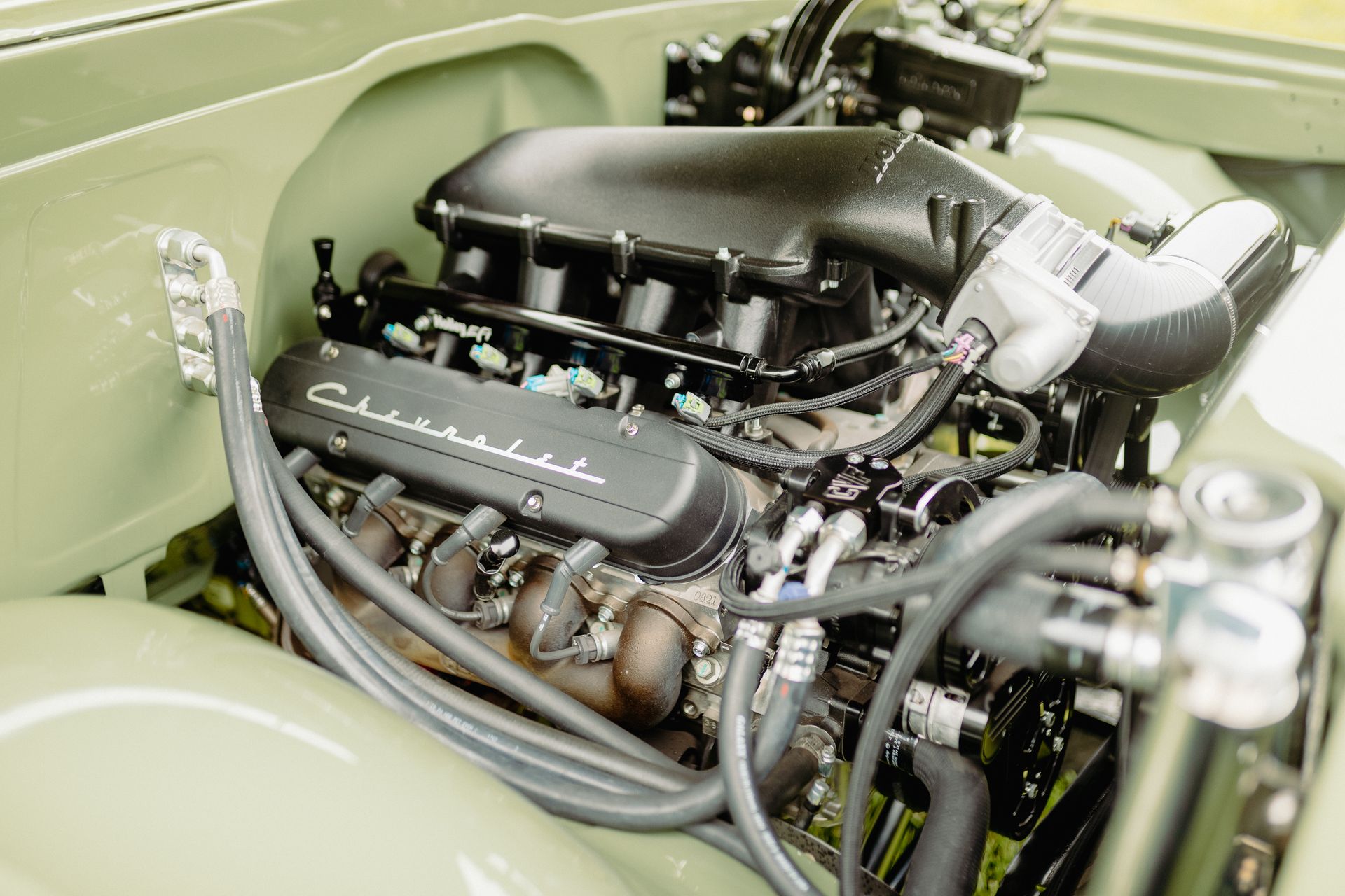 Close-up of a classic car engine bay with a black engine and olive green body panels