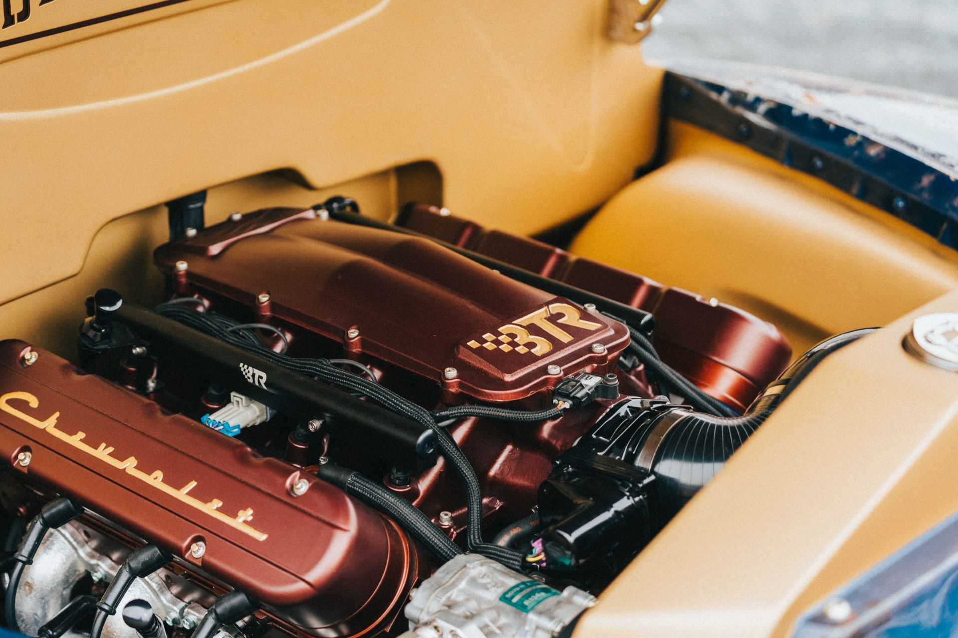 Close-up of a custom engine bay with maroon components and chrome parts in a beige car interior