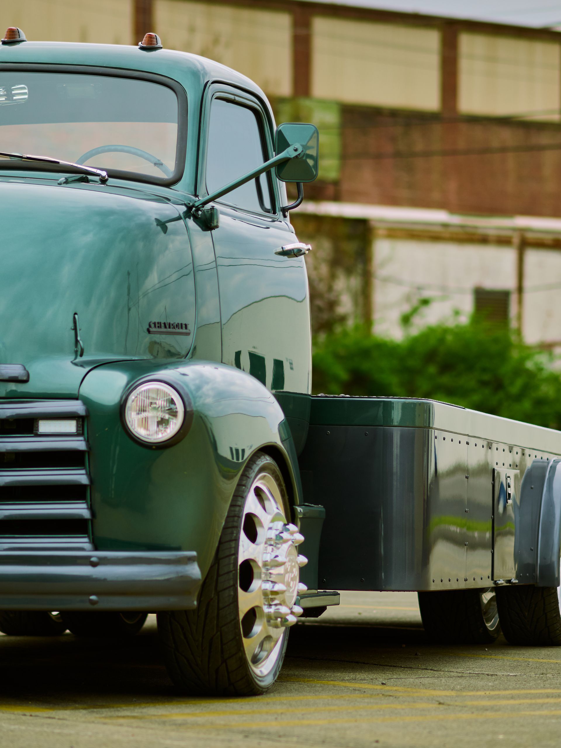 Vintage green pickup truck with a trailer parked outdoors near a building.