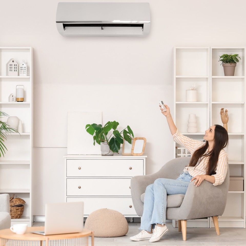 Woman using AC remote in a white room with bookshelves.