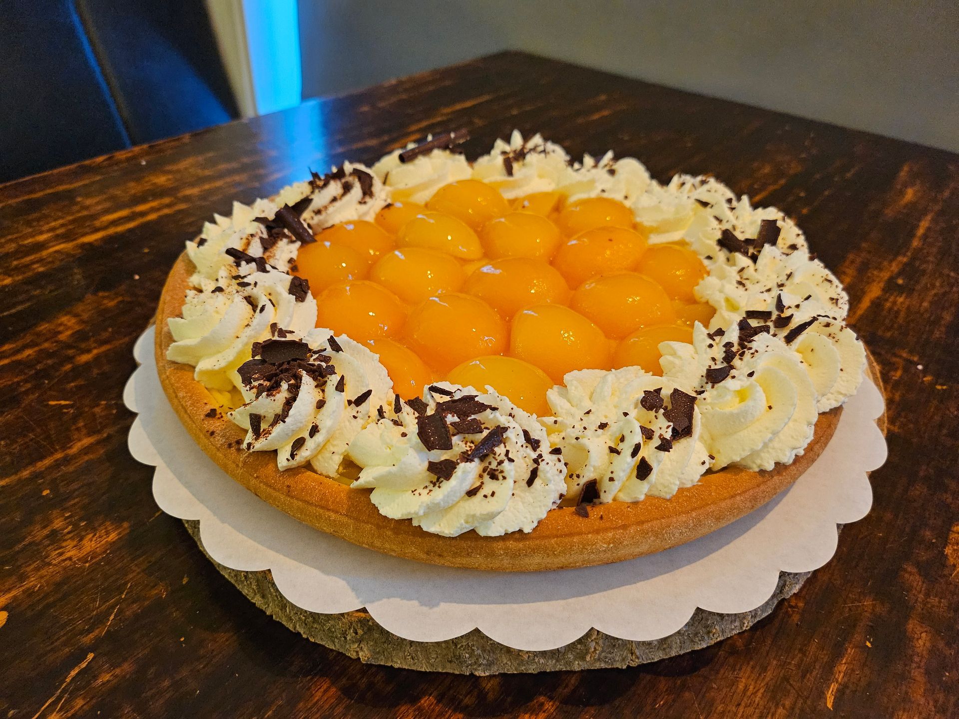 Een ronde vruchtentaart, bedekt met sinaasappelpartjes en slagroomkrullen, bestrooid met chocoladeschaafsel.