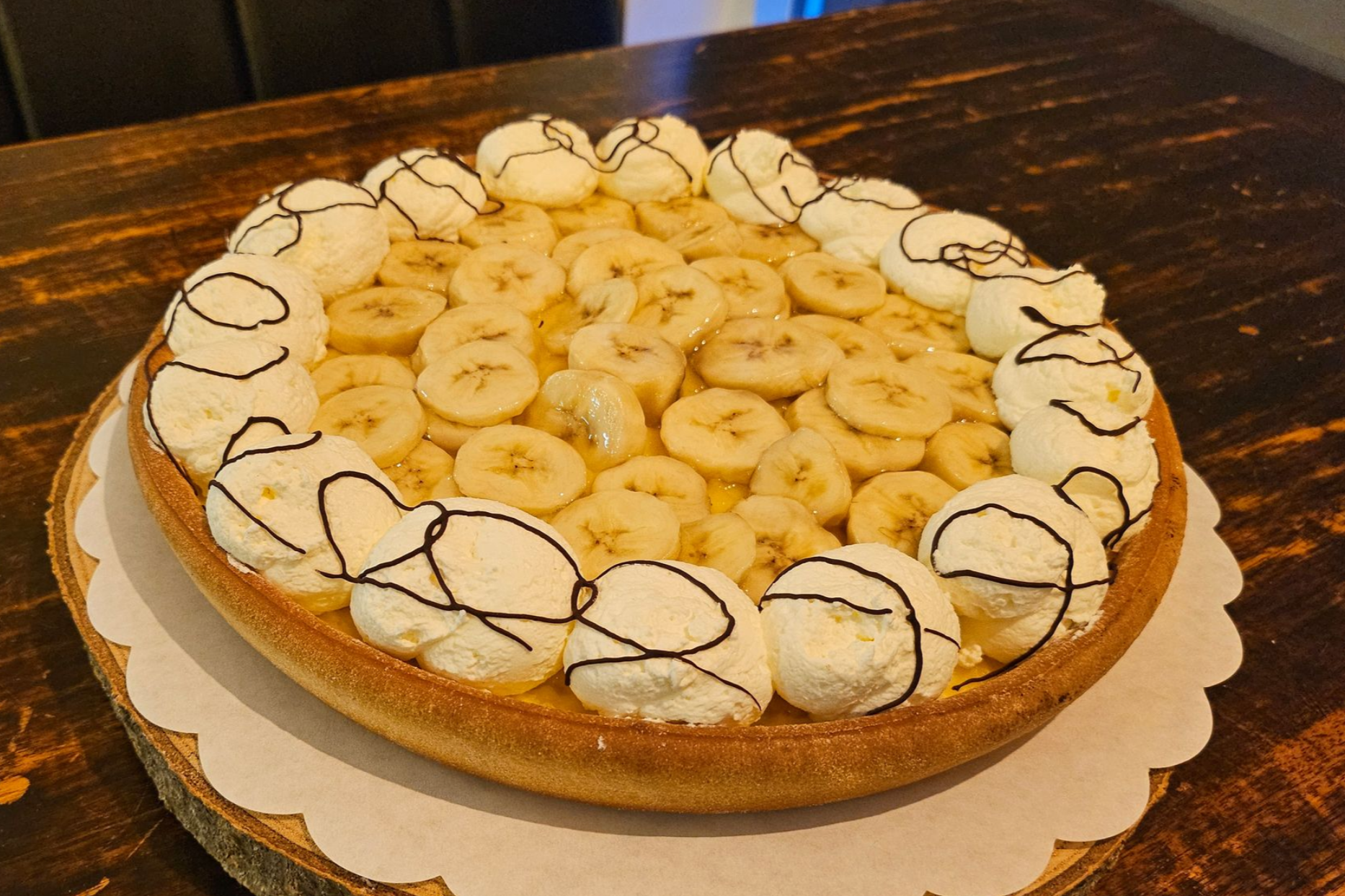 Bananentaart met plakjes banaan op een bodem, versierd met toefjes slagroom besprenkeld met chocolade.