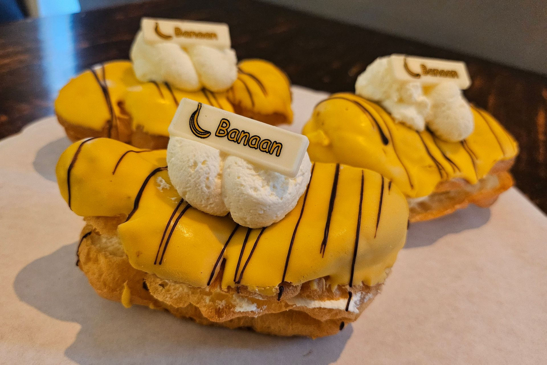 Drie gele soezen met bananensmaak, gegarneerd met witte slagroom en een klein stukje merkchocolade.