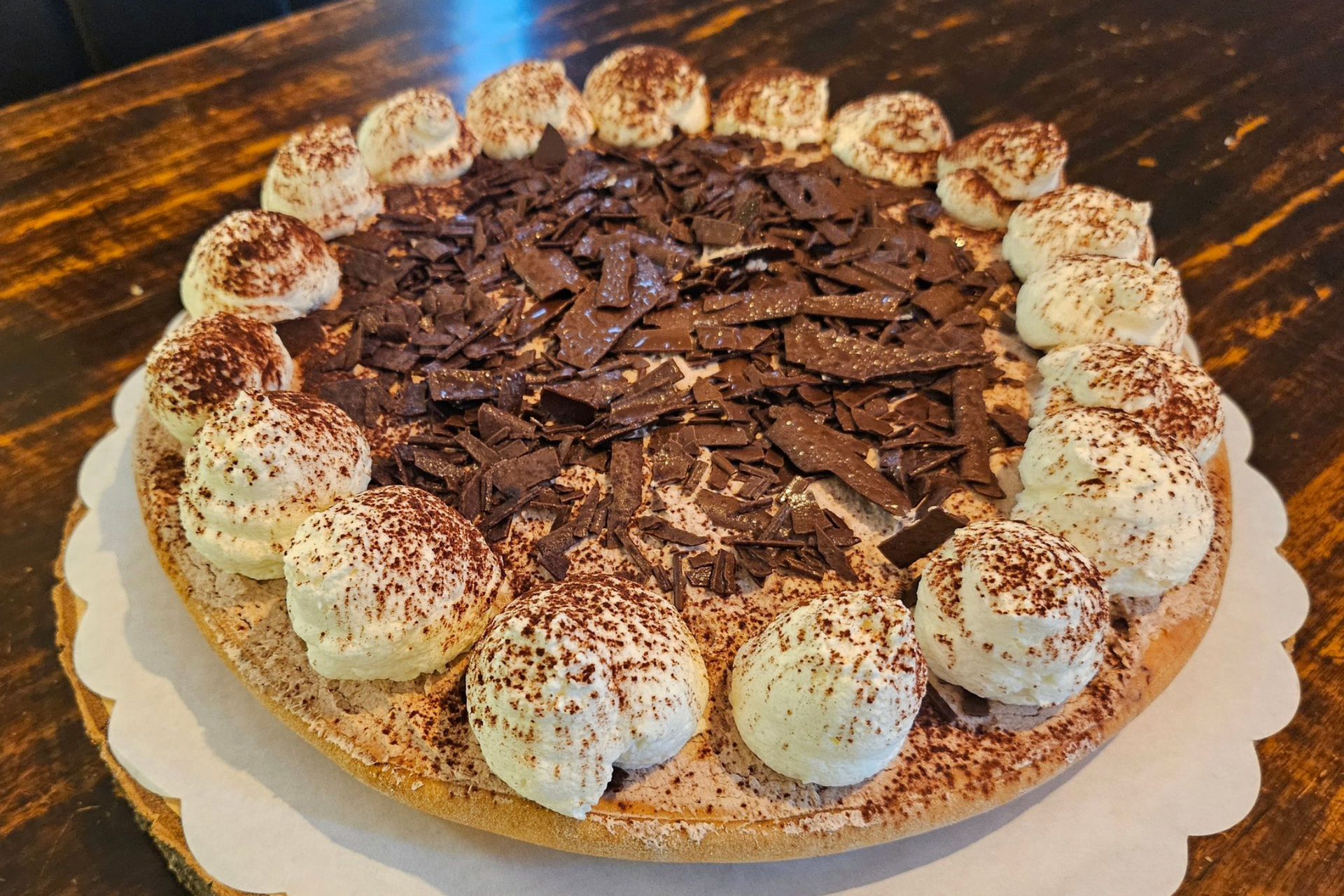 Een ronde chocoladeroomtaart, gegarneerd met toefjes slagroom en chocoladeschaafsel.