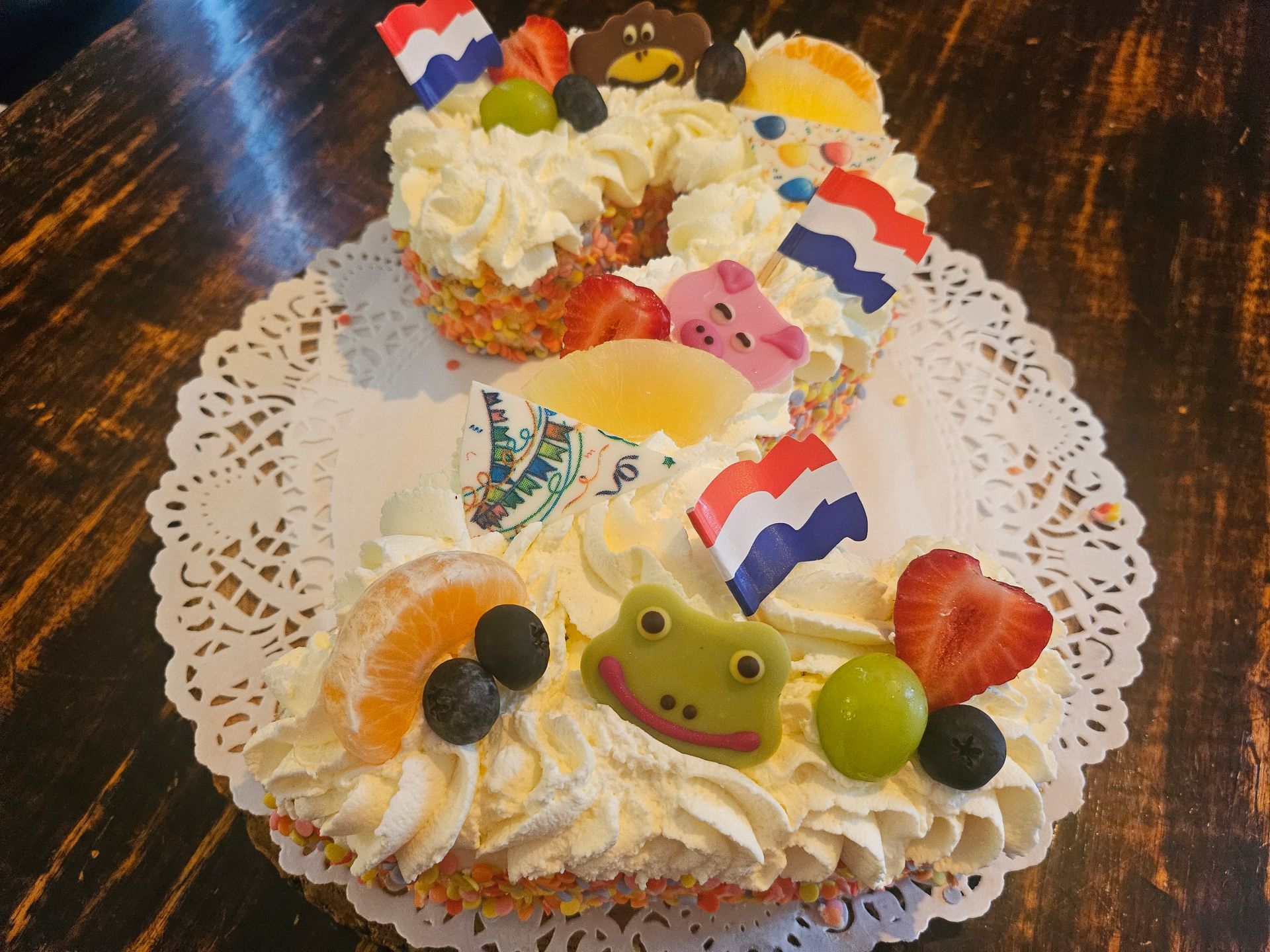 Versierde verjaardagstaart met slagroom, fruit en kleurrijke vlaggetjes.