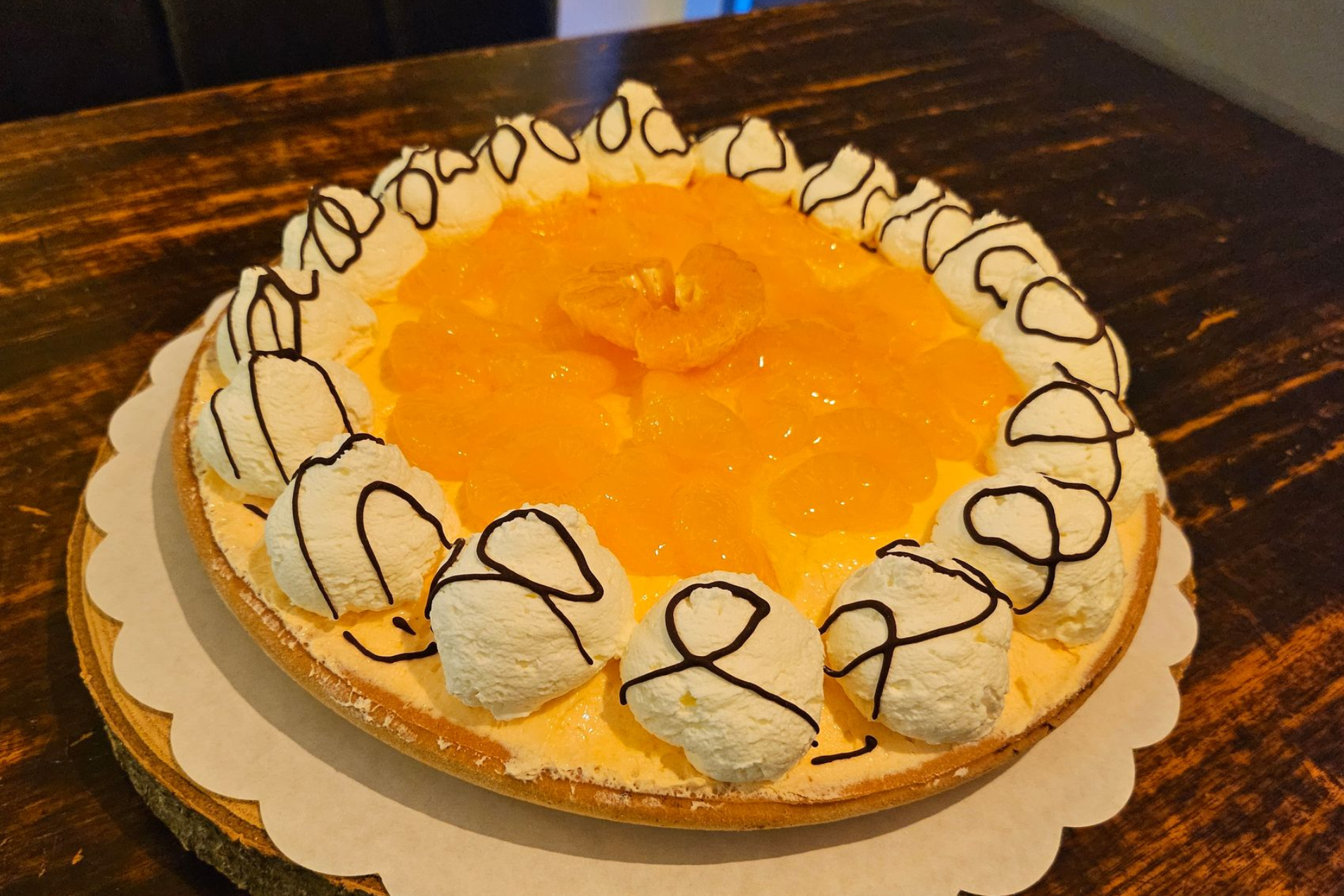 Een ronde fruittaart, gegarneerd met mandarijnpartjes, toefjes slagroom en een laagje pure chocolade.