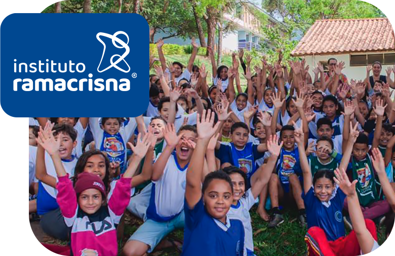 A group of over thirty children from Instituto Ramacrisna smiling with their arms raised up in the air.