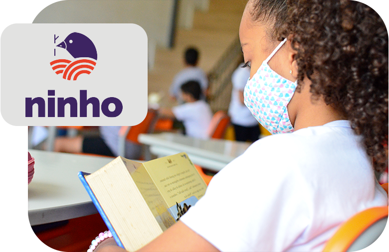 A masked girl, sitting at a table reading a book representing Projeto Ninho.