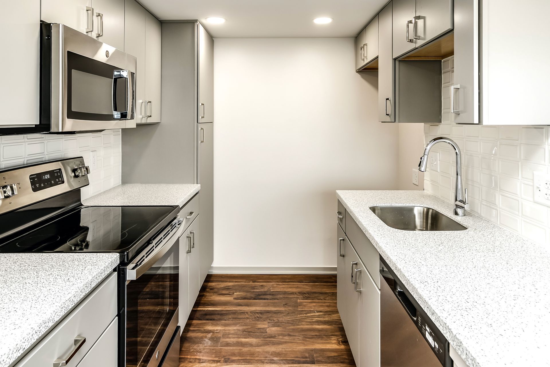 Modern white kitchen with stainless steel appliances, granite countertops, and wood flooring