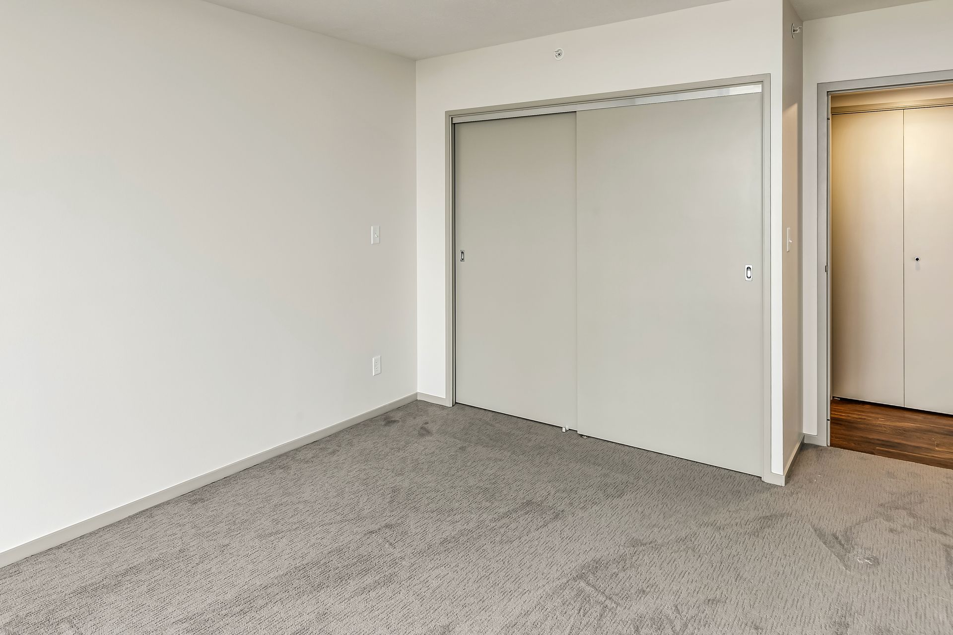 Empty carpeted bedroom with white walls and a mirrored closet door