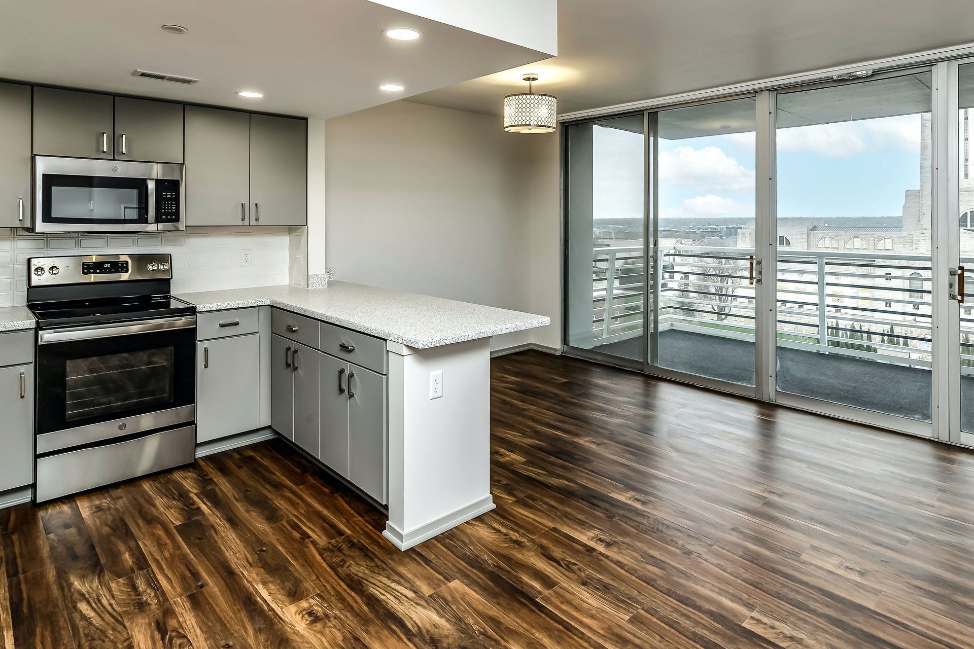 Modern kitchen with stainless appliances, white island, wood floors, and sliding glass doors to a balcony with city view