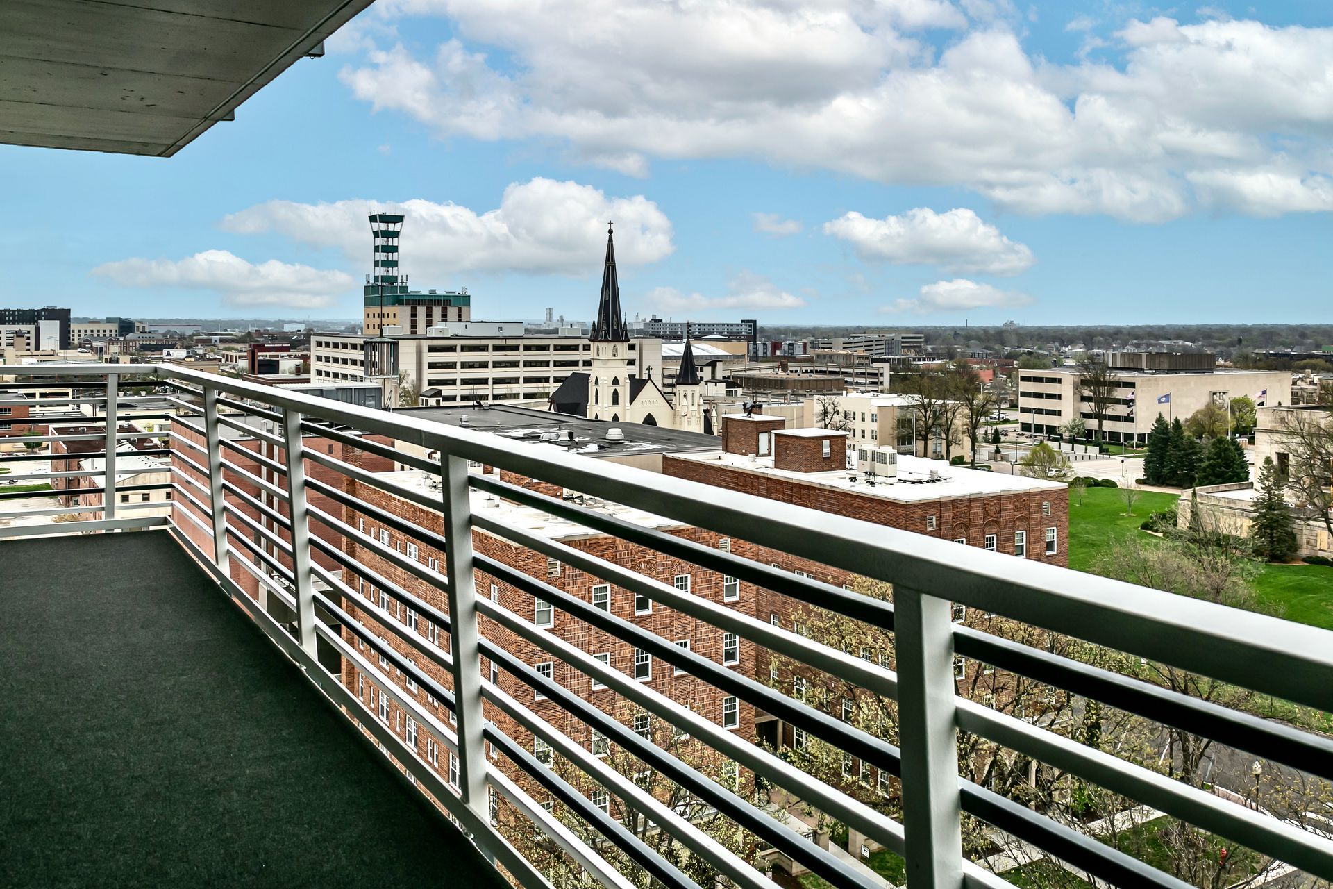 City skyline and church spires viewed from a balcony with metal railing under a blue sky.