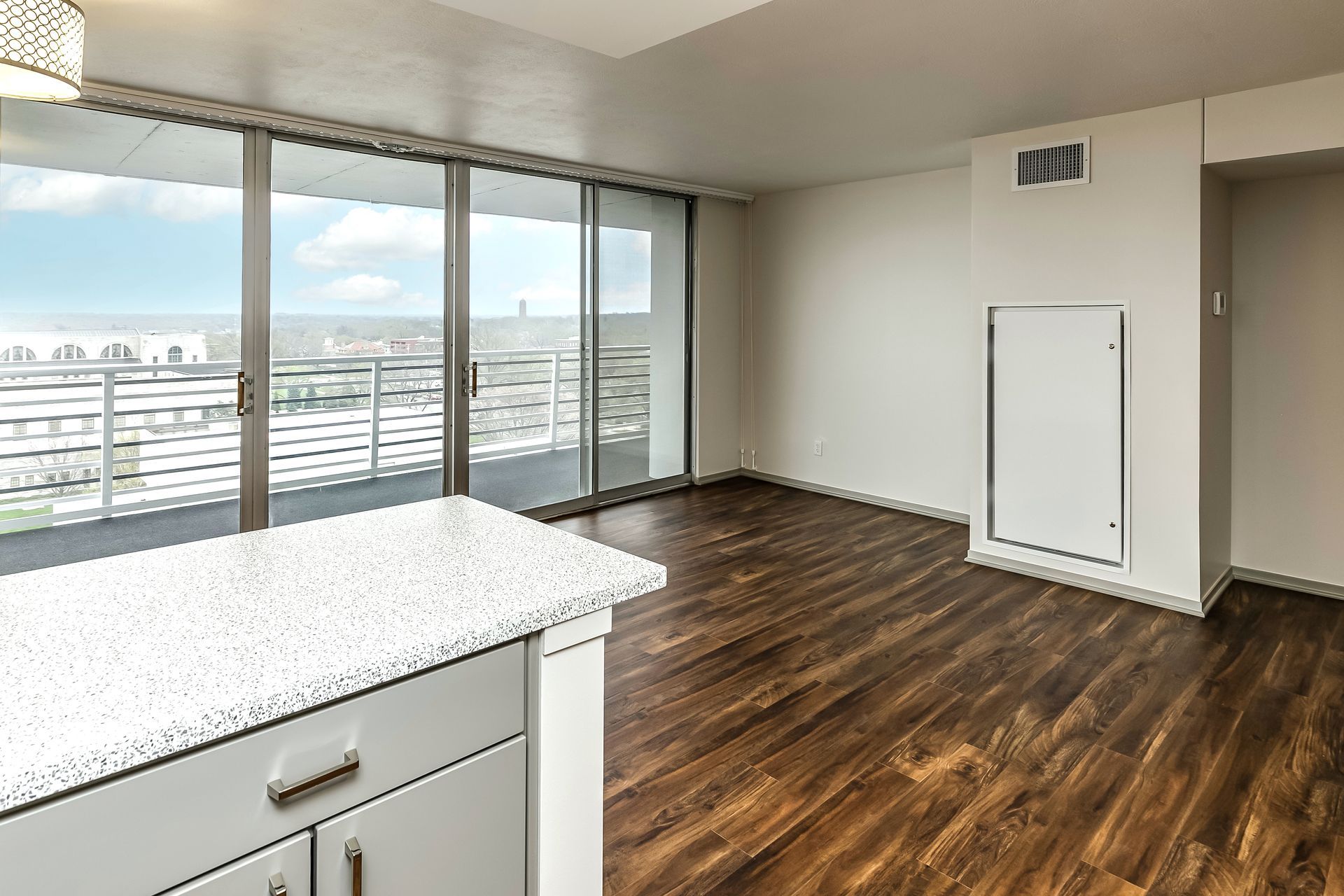 Empty modern apartment interior with large windows, dark wood floors, and white kitchen counter